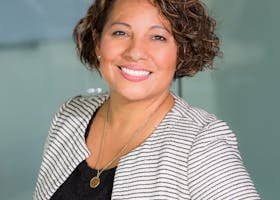 A confident woman with curly hair smiling in an office environment, conveying professionalism and approachability.